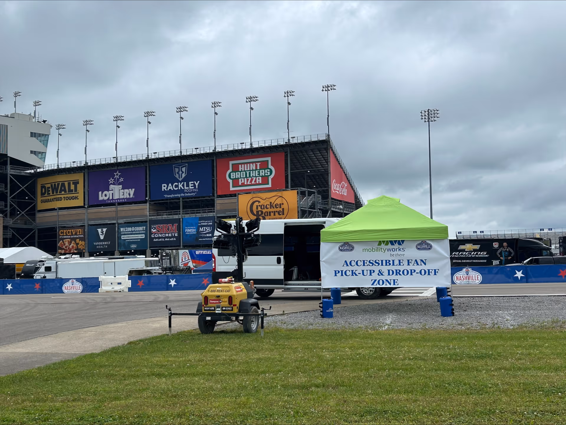Outdoor event space near stadium wall with sponsor banners, a green tent, and a white van.