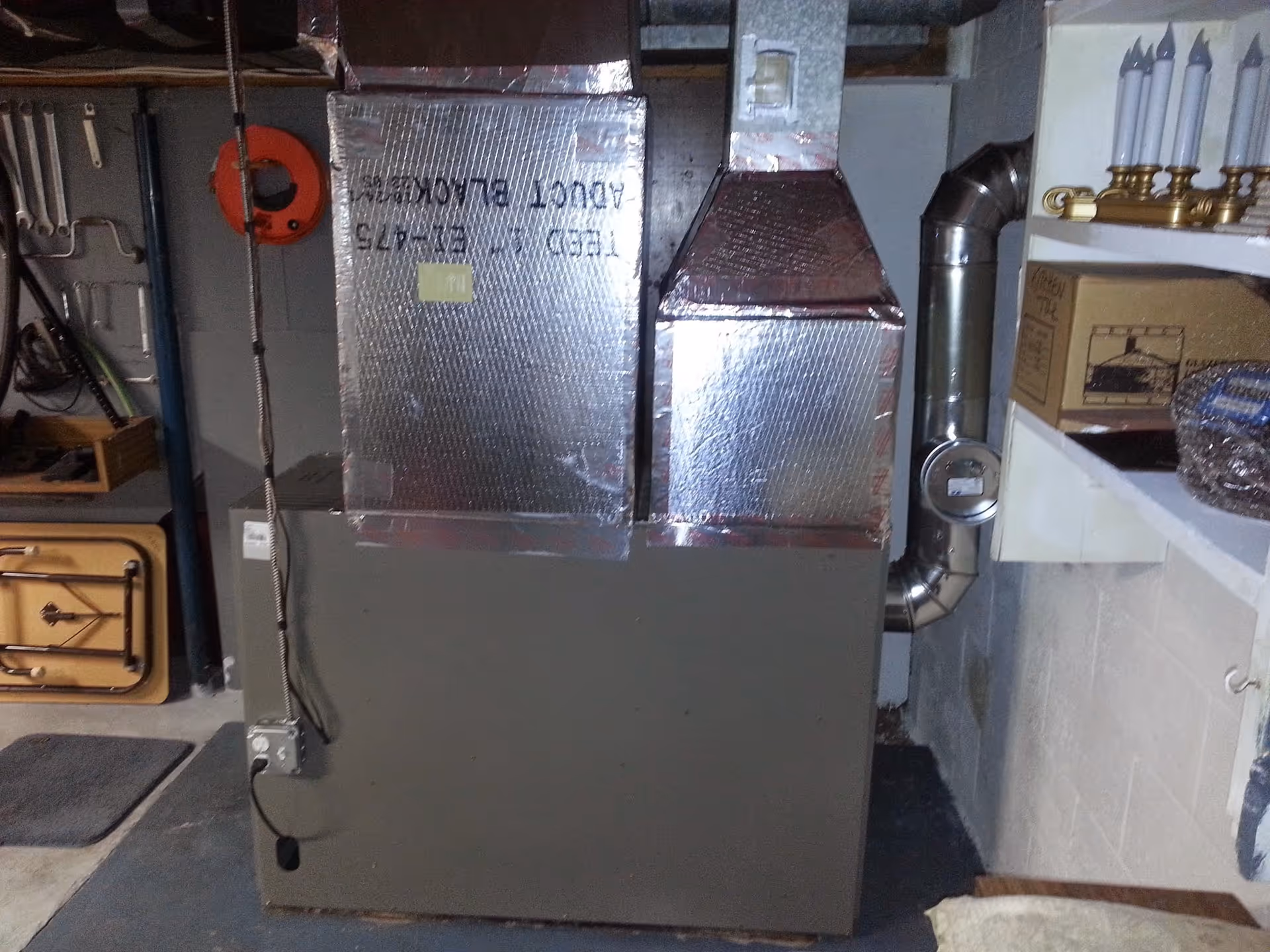 Basement mechanical room with a large furnace, silver ductwork, and pipes