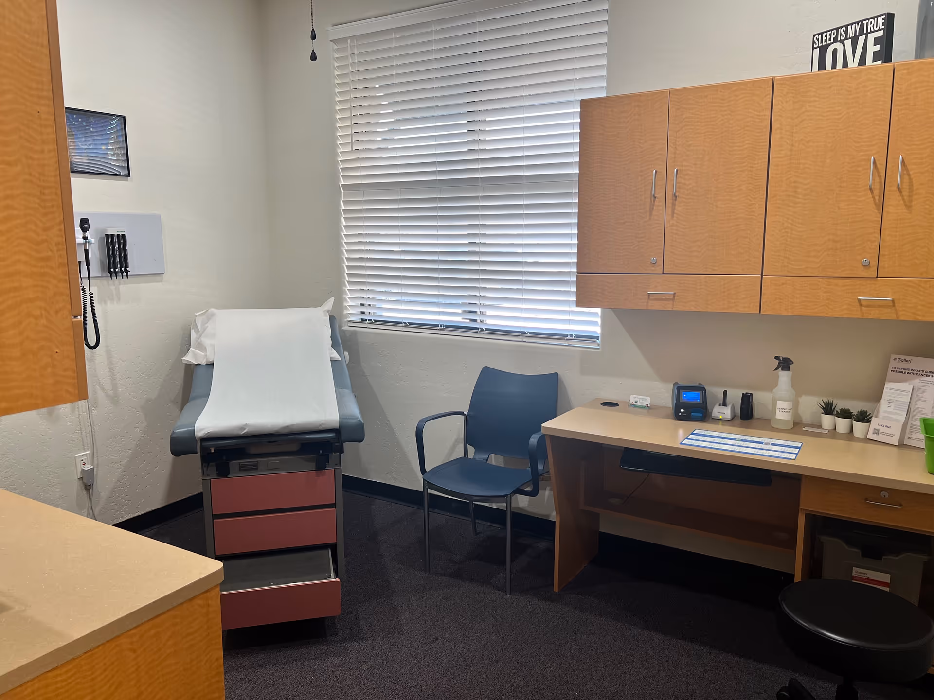 A medical examination room in a senior care facility with a chair, desk, and cabinets.