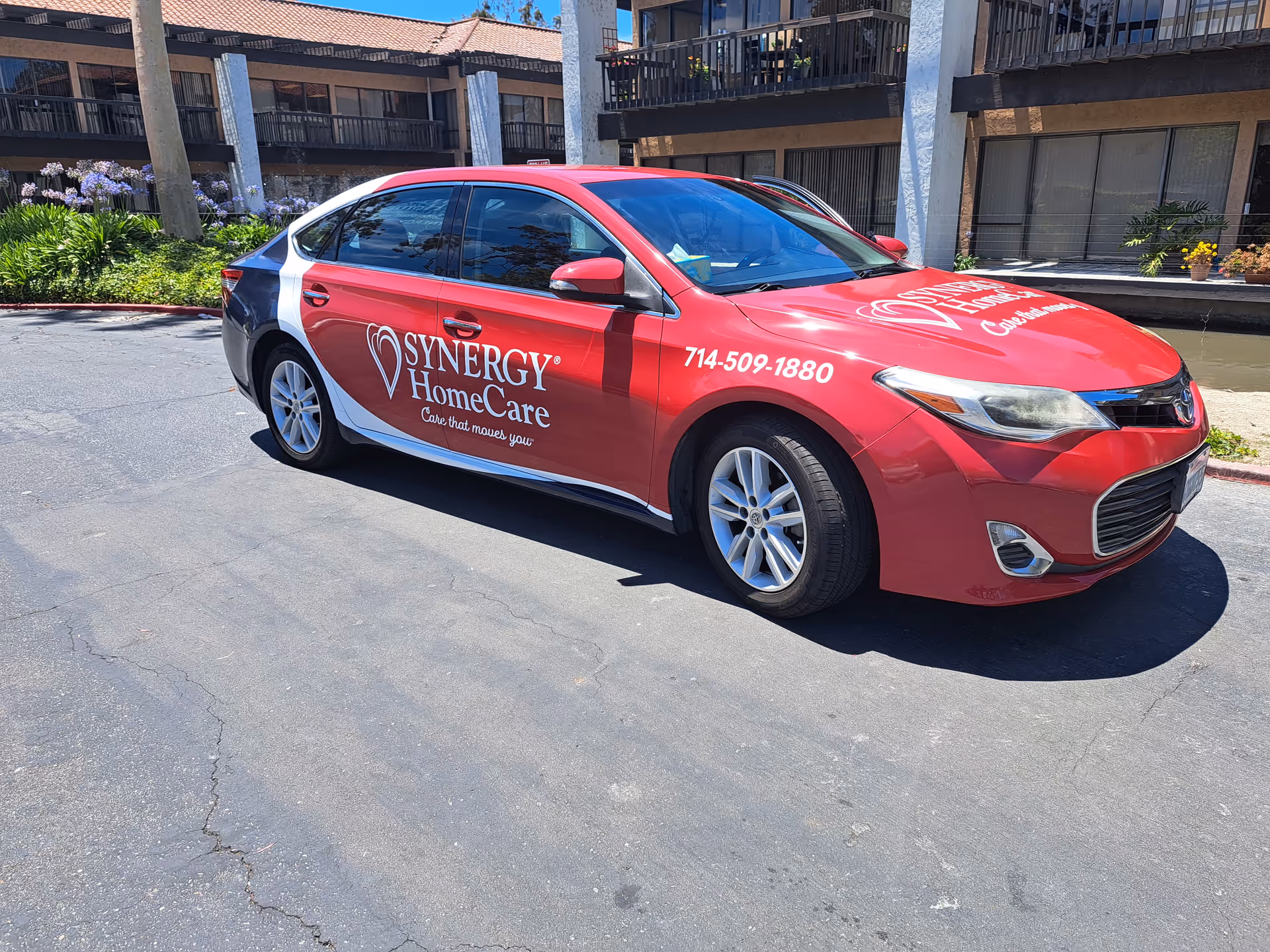 Red SYNERGY HomeCare car parked in a lot with a building behind.