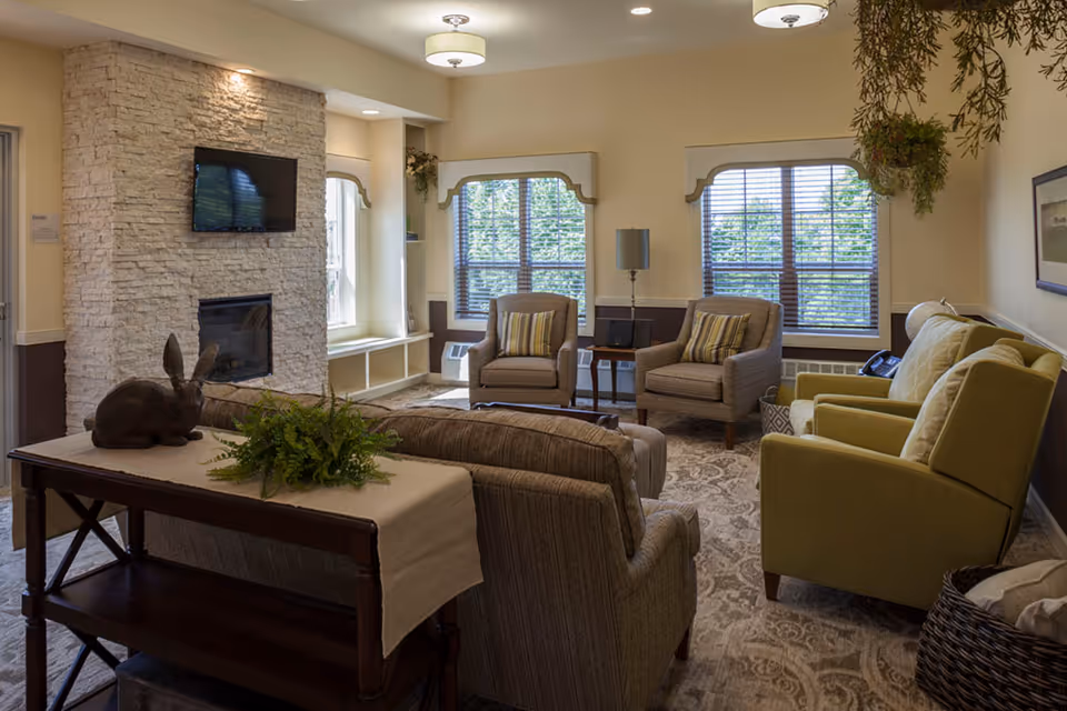 Cozy common living room with a stone fireplace, sofas, chairs, and windows.