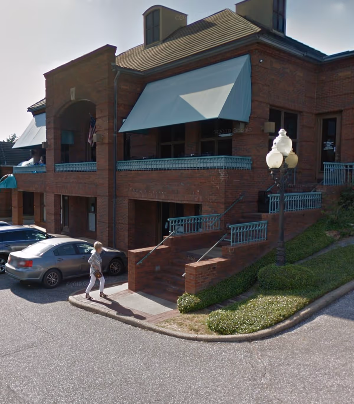Brick senior living building exterior with blue awnings, stairs, and a person walking nearby.