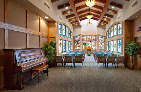 Chapel-like indoor gathering room with wooden beams, stained glass windows, and arranged chairs.