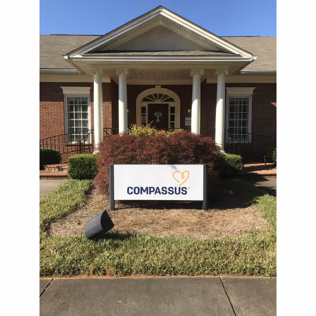 Front view of a Compassus facility entrance with a sign and trimmed shrubs.