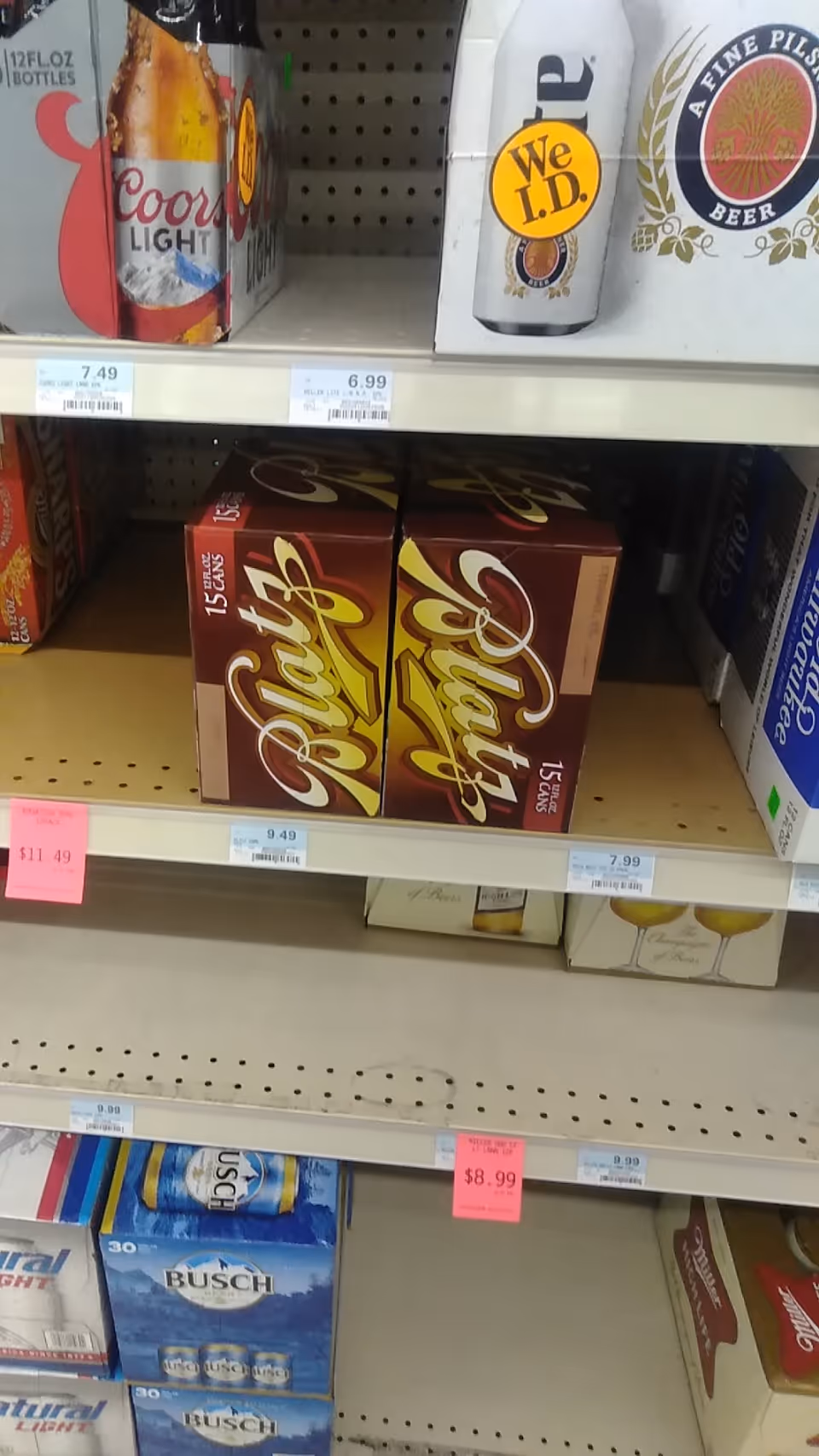 Store aisle with beer boxes stacked on shelves and price tags visible.