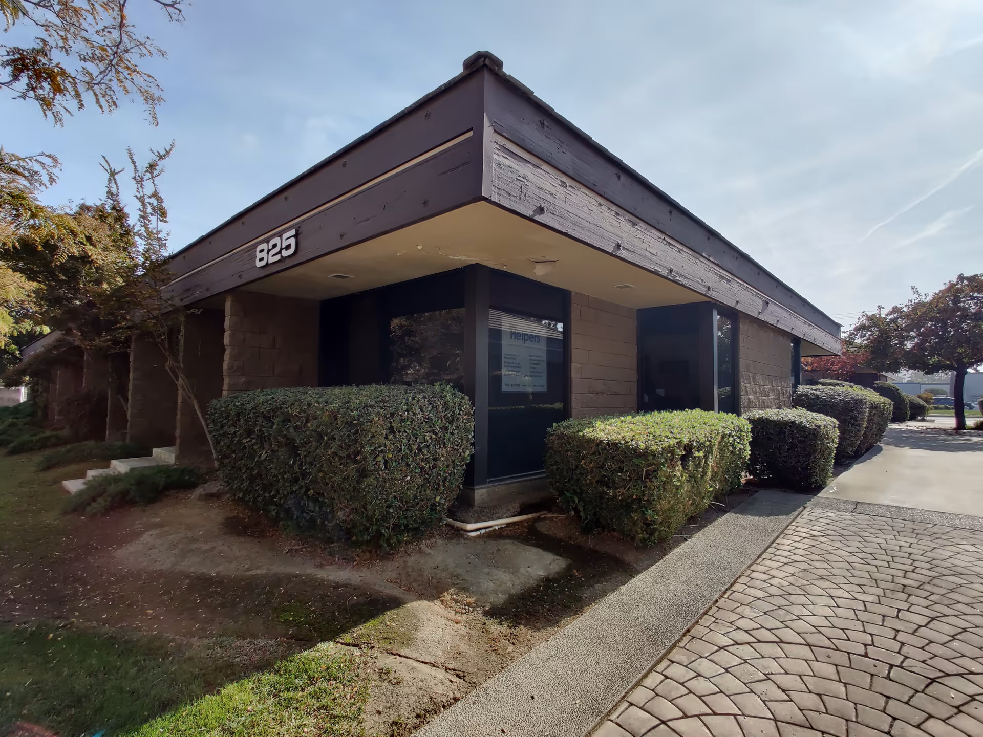 Front view of a single-story building with trimmed hedges and a cobblestone walkway