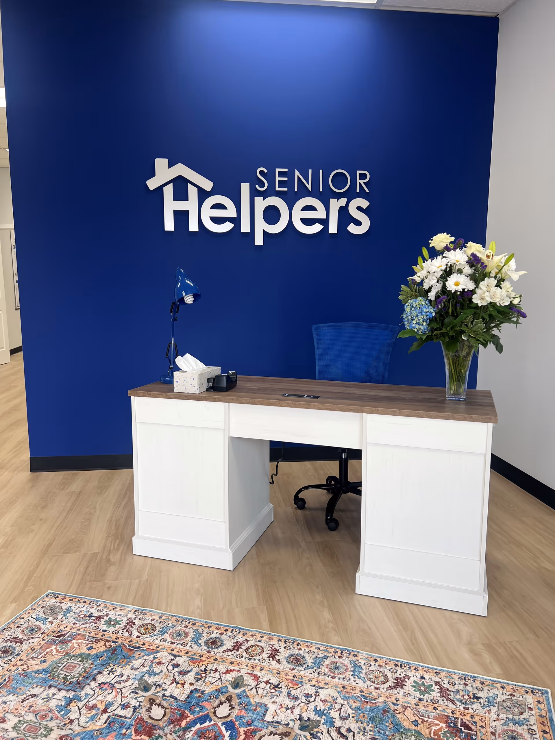 Reception desk in a Senior Helpers lobby featuring a blue wall with logo and flowers.