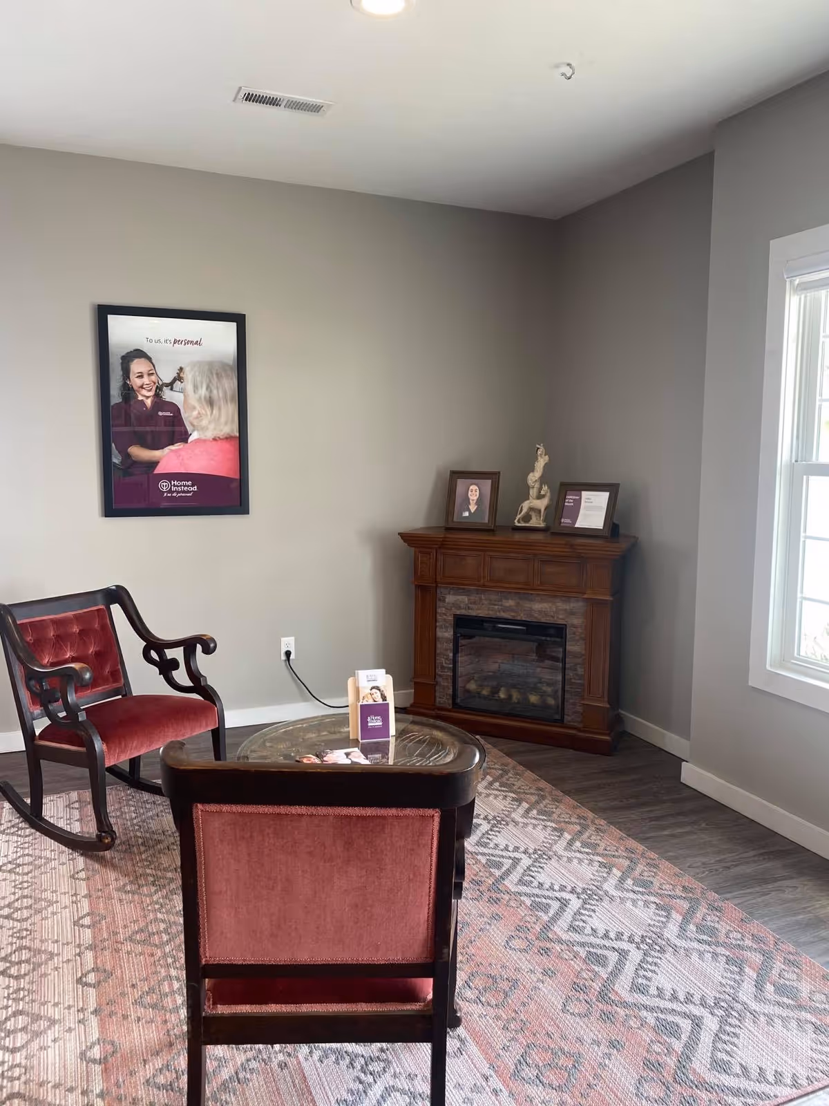 A cozy senior living lounge with red chairs, a glass coffee table, and a fireplace.