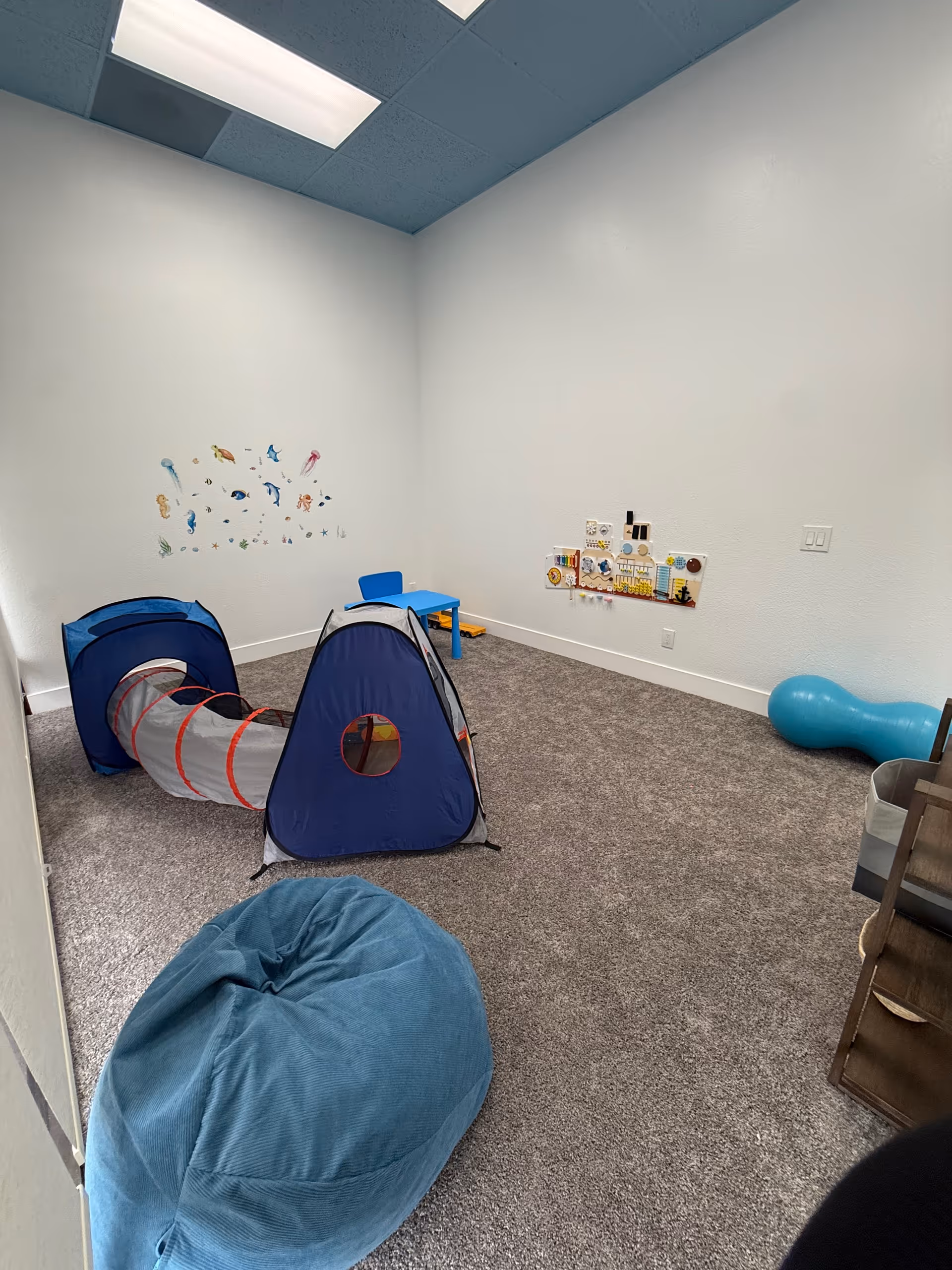Small interior playroom with tunnel tent, blue bean bag, and wall decals.