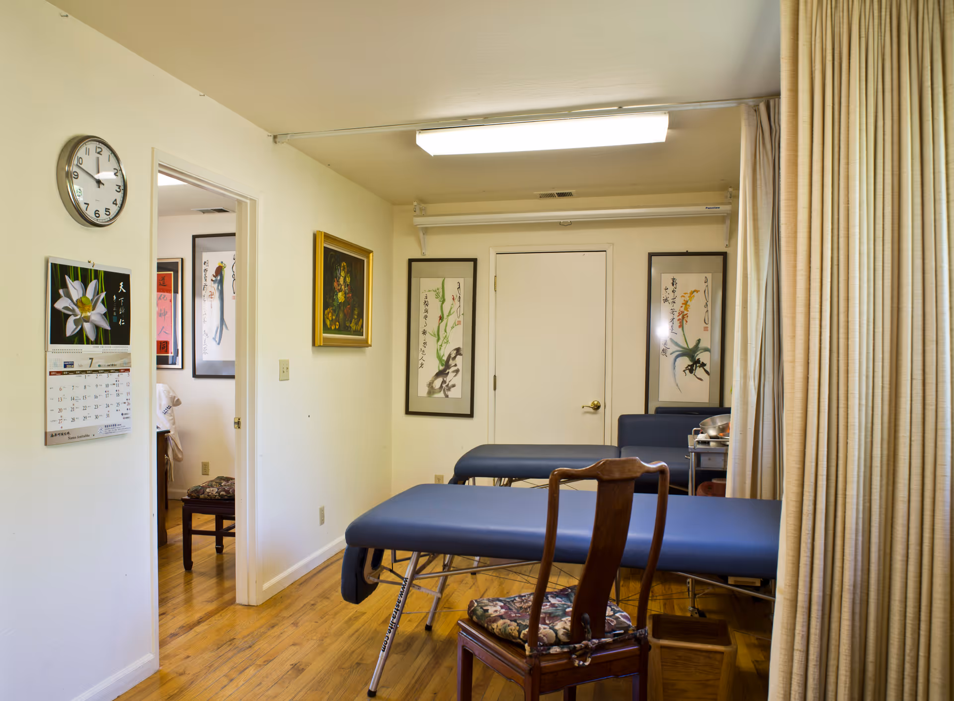 A medical treatment room with blue examination bed, curtains, and wall art.