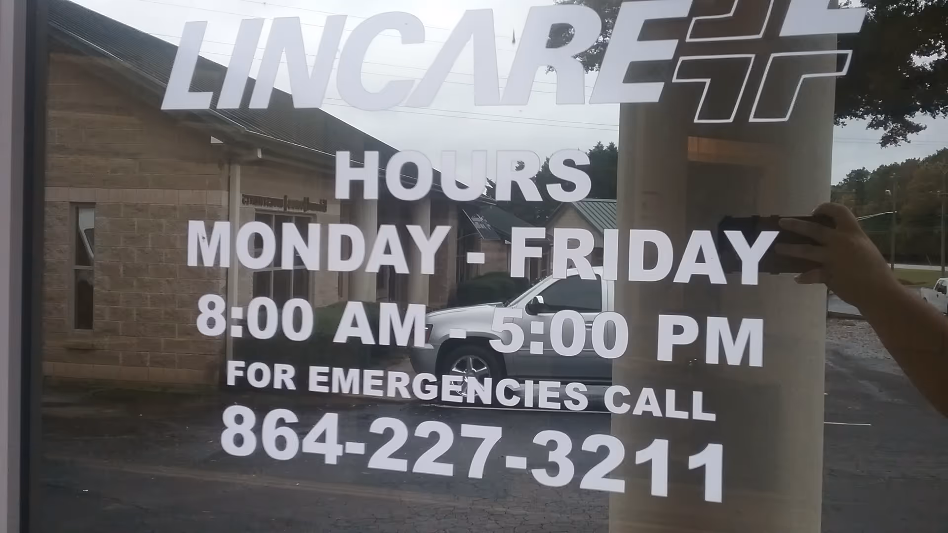Glass storefront window displays LINCARE hours with a reflection of a car.
