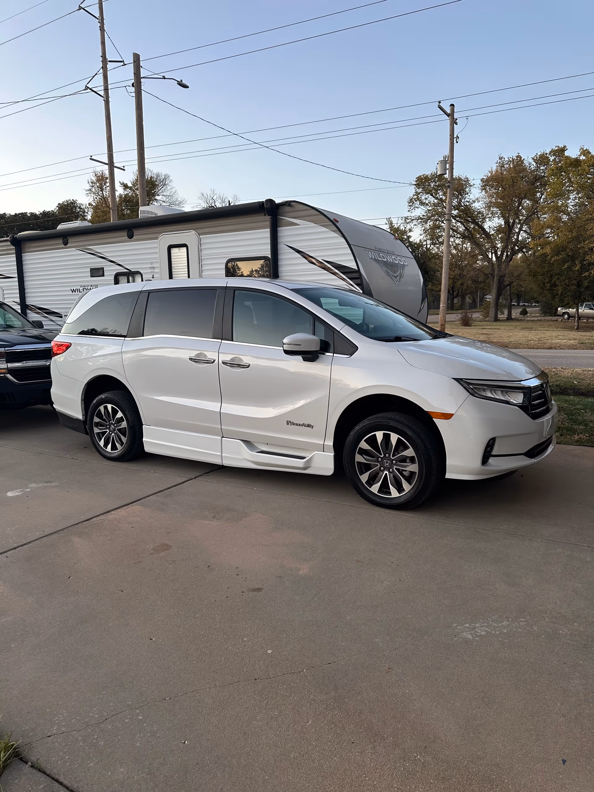 White wheelchair-accessible minivan parked beside a travel trailer outdoors.