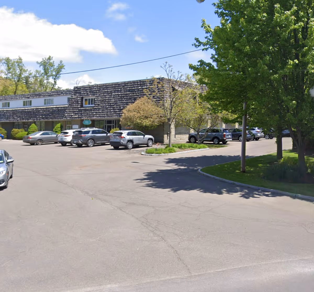 Exterior view of a Home Instead facility with parked cars and surrounding trees.