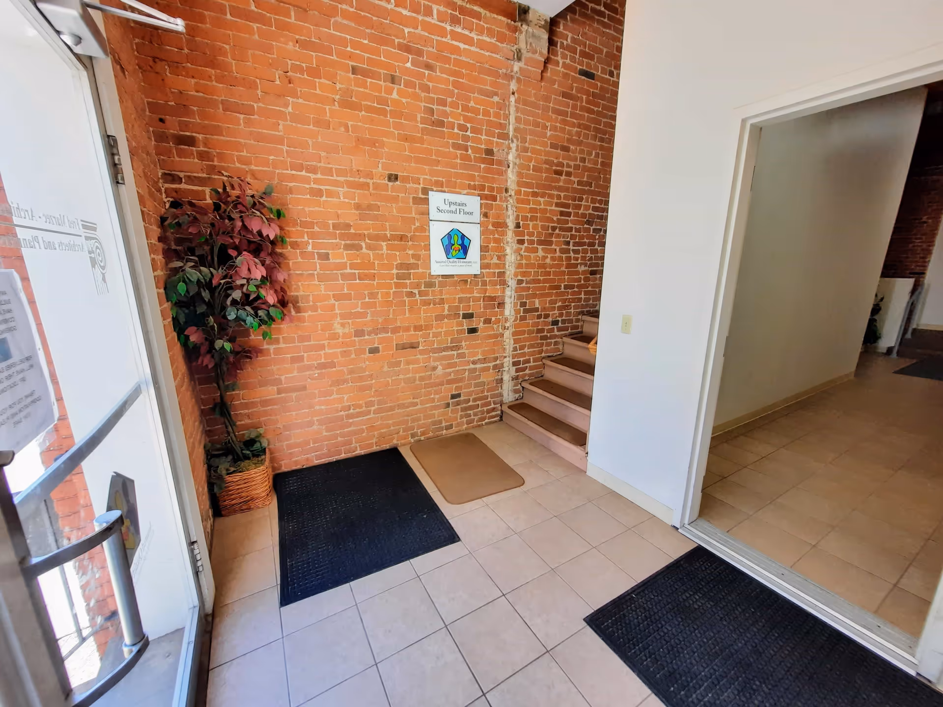 Interior entrance area with brick wall, staircase, potted plant, and signs for upstairs second floor.