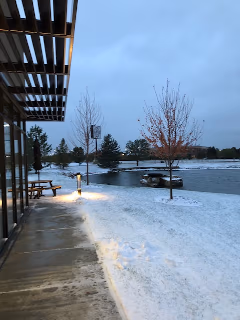 Snowy outdoor area beside a building with a picnic table and leafless trees.