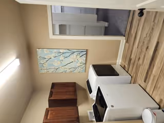 Interior kitchenette in senior living unit with white appliances, wood cabinets, and wall art.