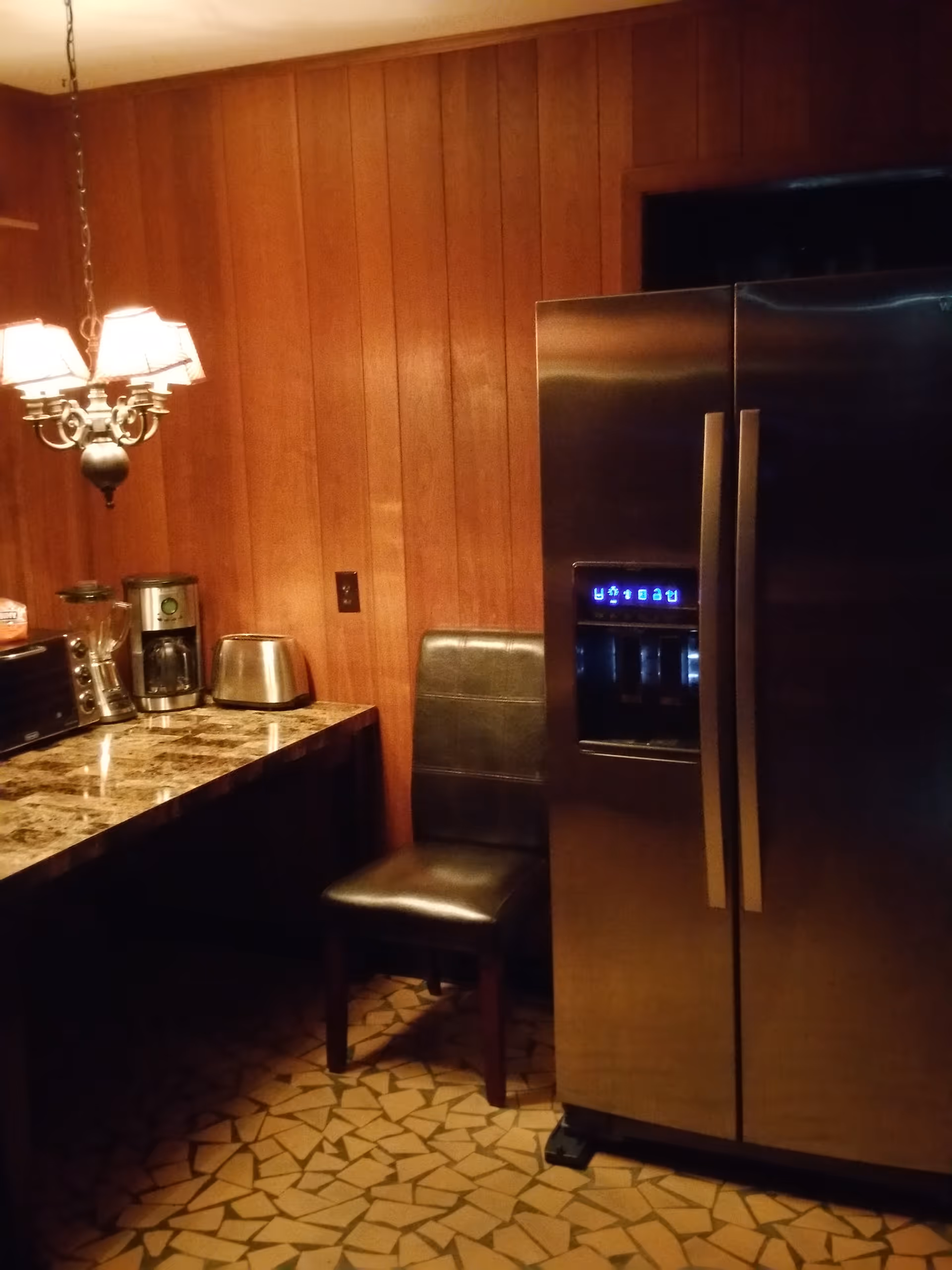 Wood-paneled kitchen area with stainless refrigerator, coffee maker, toaster, and granite countertop.