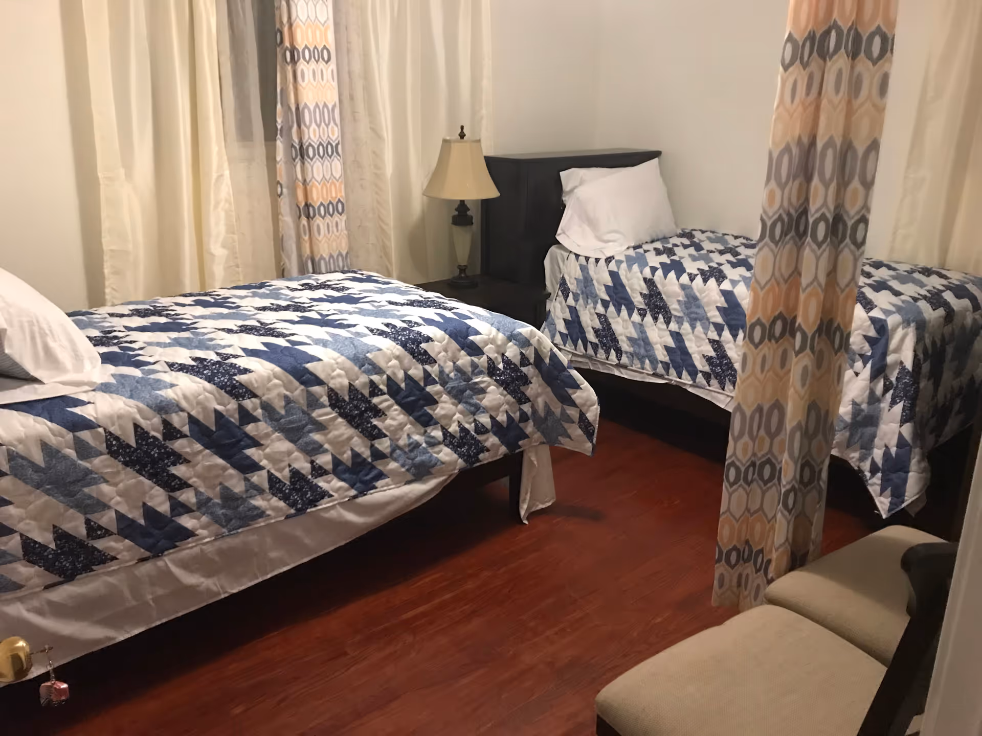 Two twin beds with blue and white patchwork quilts in a shared senior living bedroom.