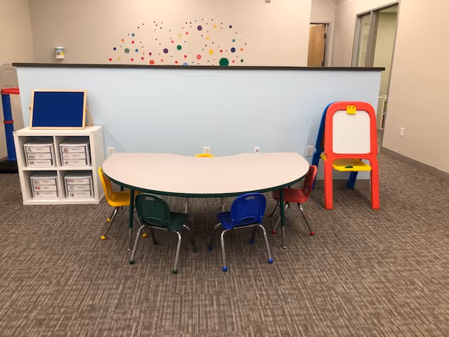 Small activity room with curved table, colorful chairs, and storage shelves in a senior living facility.