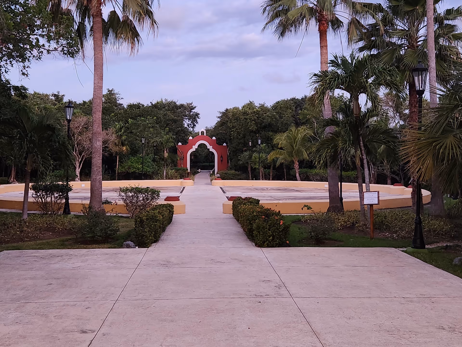 Pathway through tropical landscaping leads to a pink archway in a circular courtyard.
