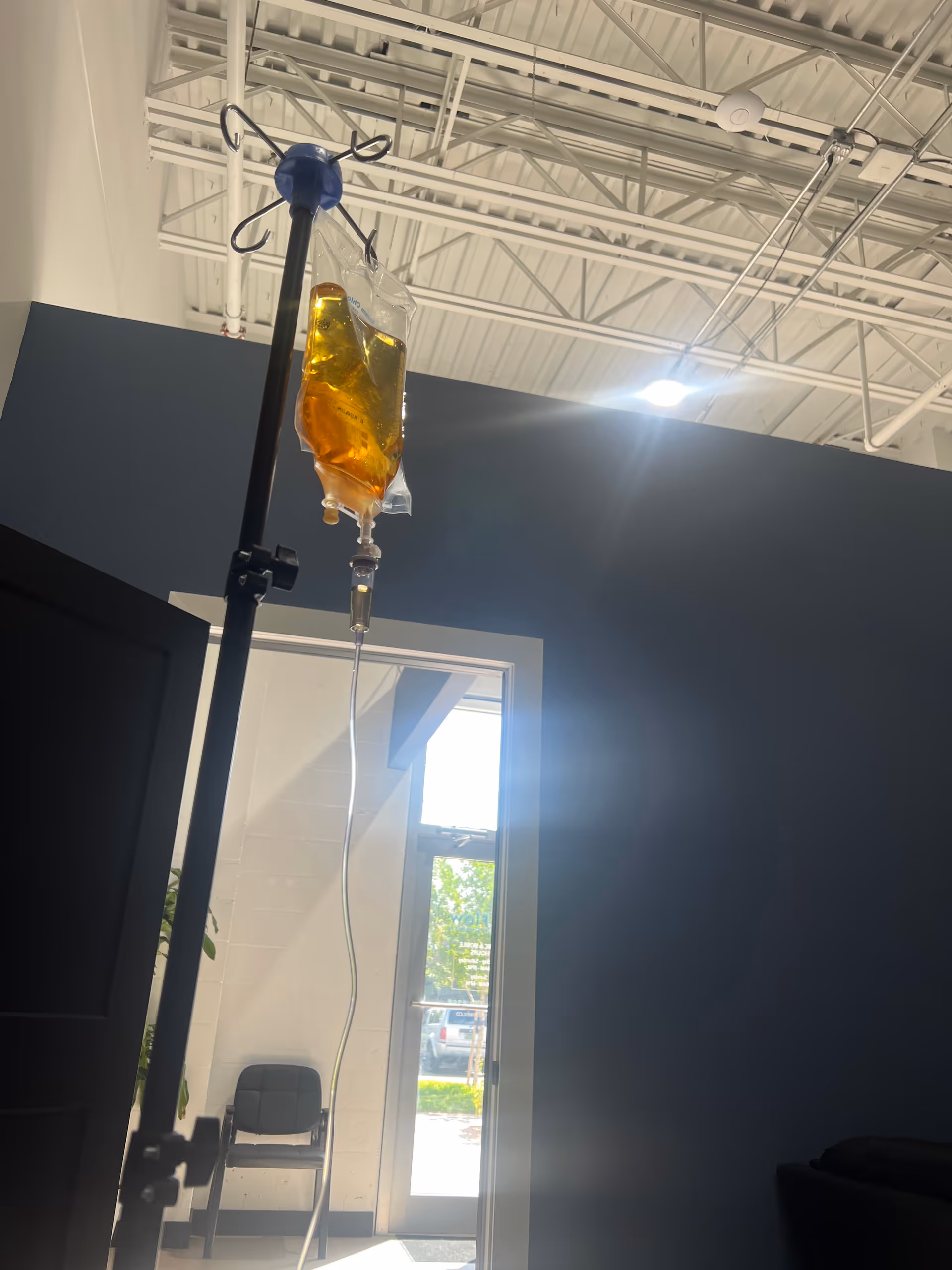 IV infusion bag on a stand inside a modern facility room with blue walls.