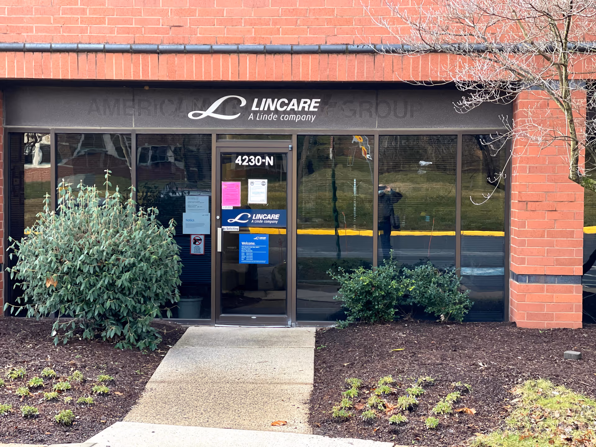 Front of LINCARE facility with glass doors, brick exterior, and landscaped entry.