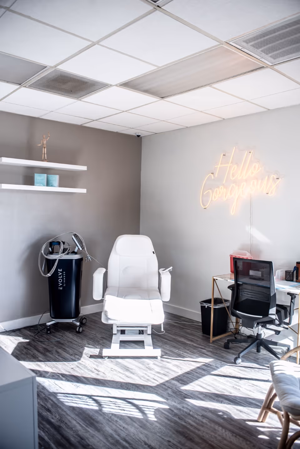 Bright IV therapy room with a white chair, neon 'Hello Gorgeous' sign, and equipment.