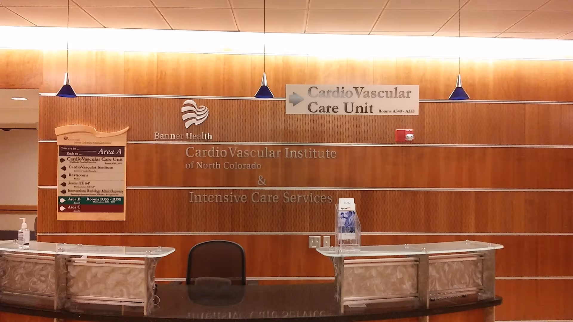 Warm wood-paneled wall with hospital signage and two front desks in a lobby.