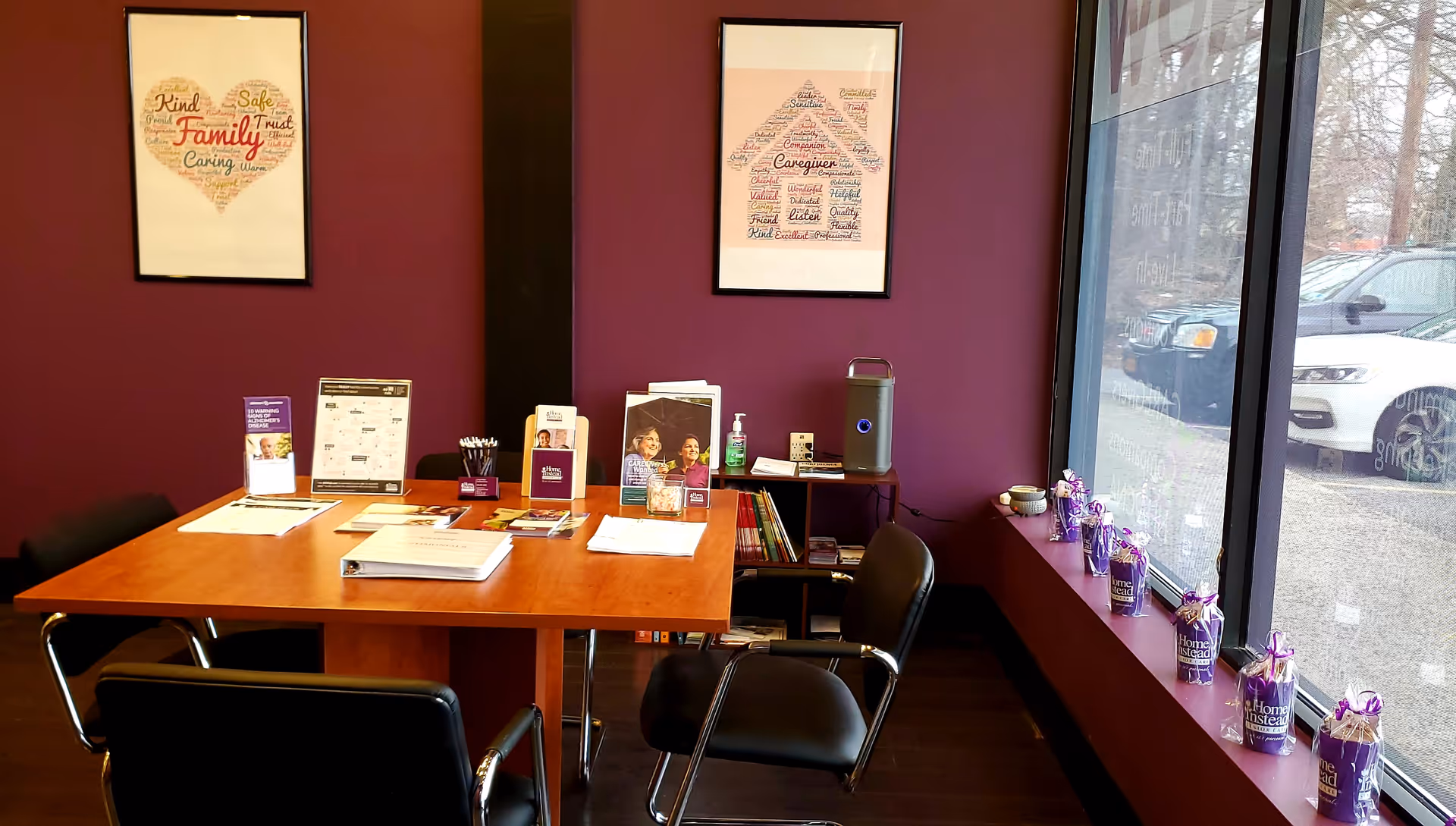 A modern reception area with a wood table, purple walls, framed art, and large windows.