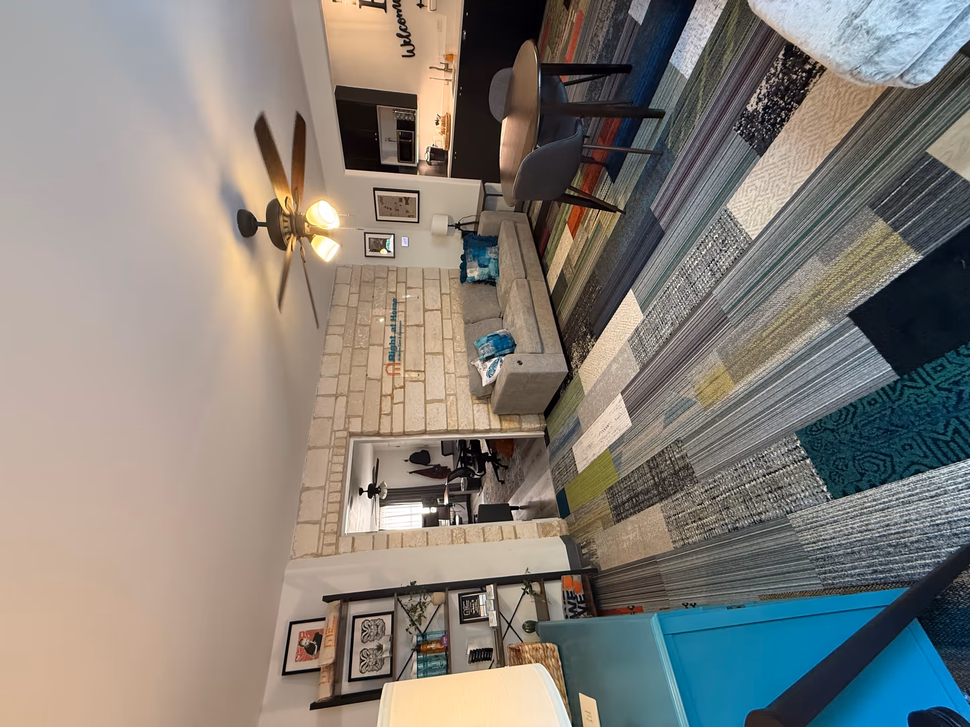 Cozy lounge area with couch, colorful rug, table, brick wall, and kitchenette.
