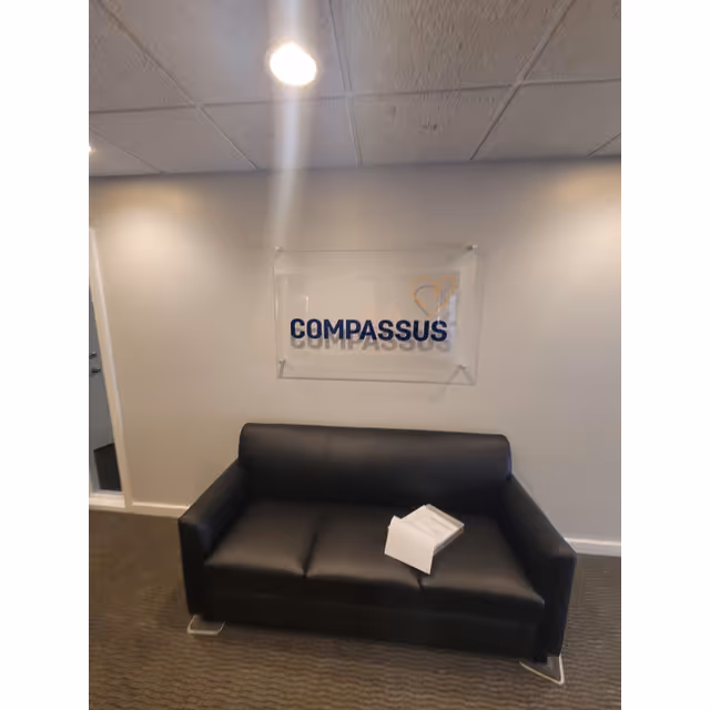 Lobby seating area with a black leather sofa and a Compassus sign on the wall.