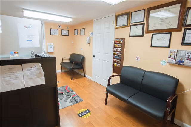 Interior reception and waiting area with black leather sofa, certificates on wall, and a magazine rack.