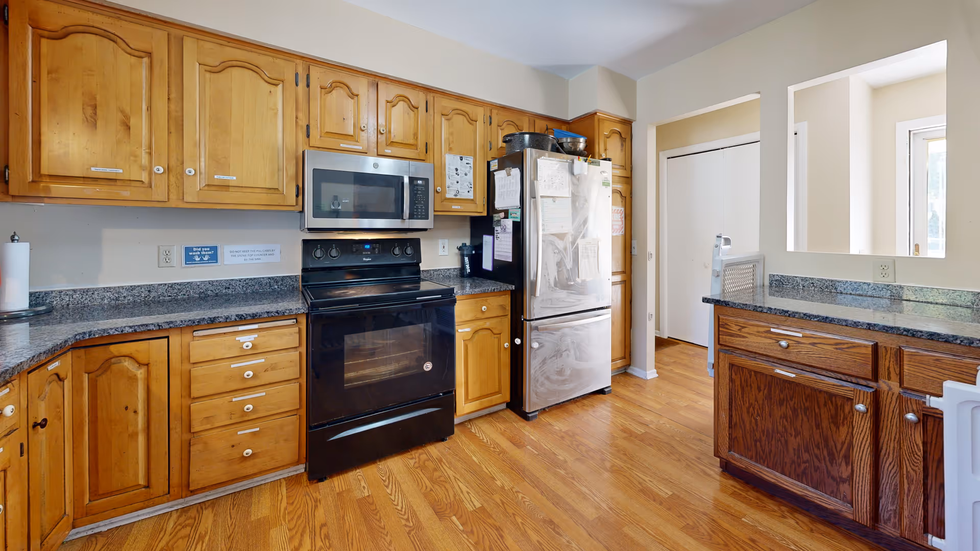 Bright kitchen with wooden cabinets, granite countertops, microwave, stove, and a stainless steel refrigerator.