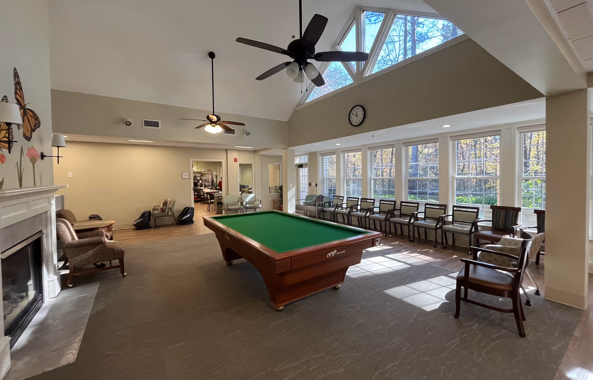 Interior common lounge with pool/billiards table, seating along windows, high ceiling with fans.