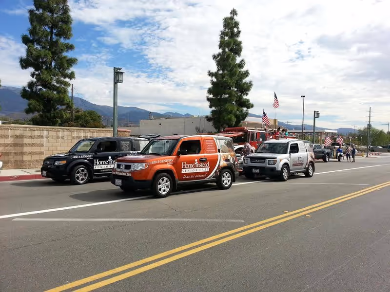 A line of Home Instead Senior Care branded vehicles parked along a street.