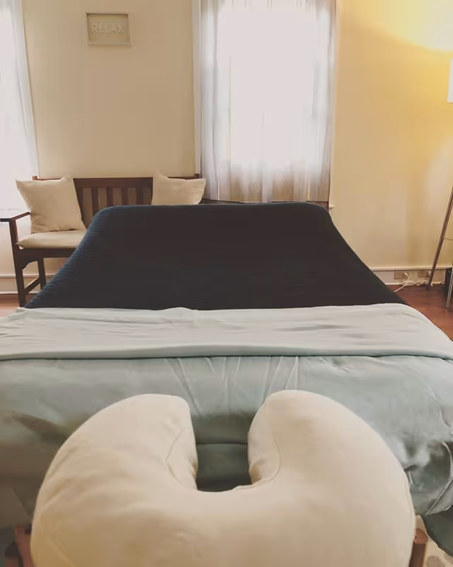 A neatly made bedroom features a bed, a bench, sheer curtains, and a 'RELAX' sign.