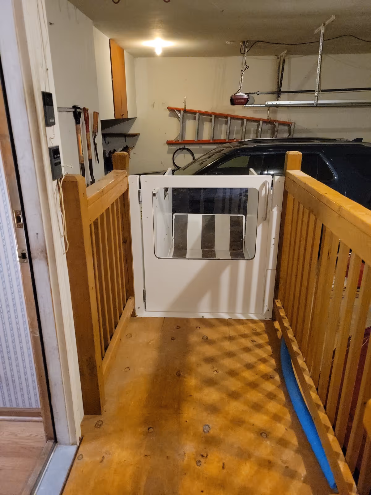 Indoor wooden walkway with a barrier gate leading to a parked car in a garage.