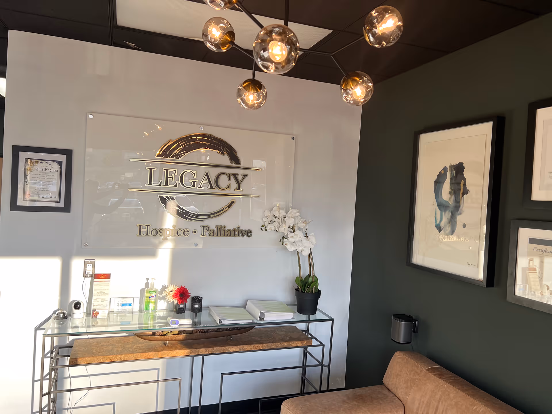 Reception area with Legacy Hospice sign, glass console table, orchid plant, and framed art.