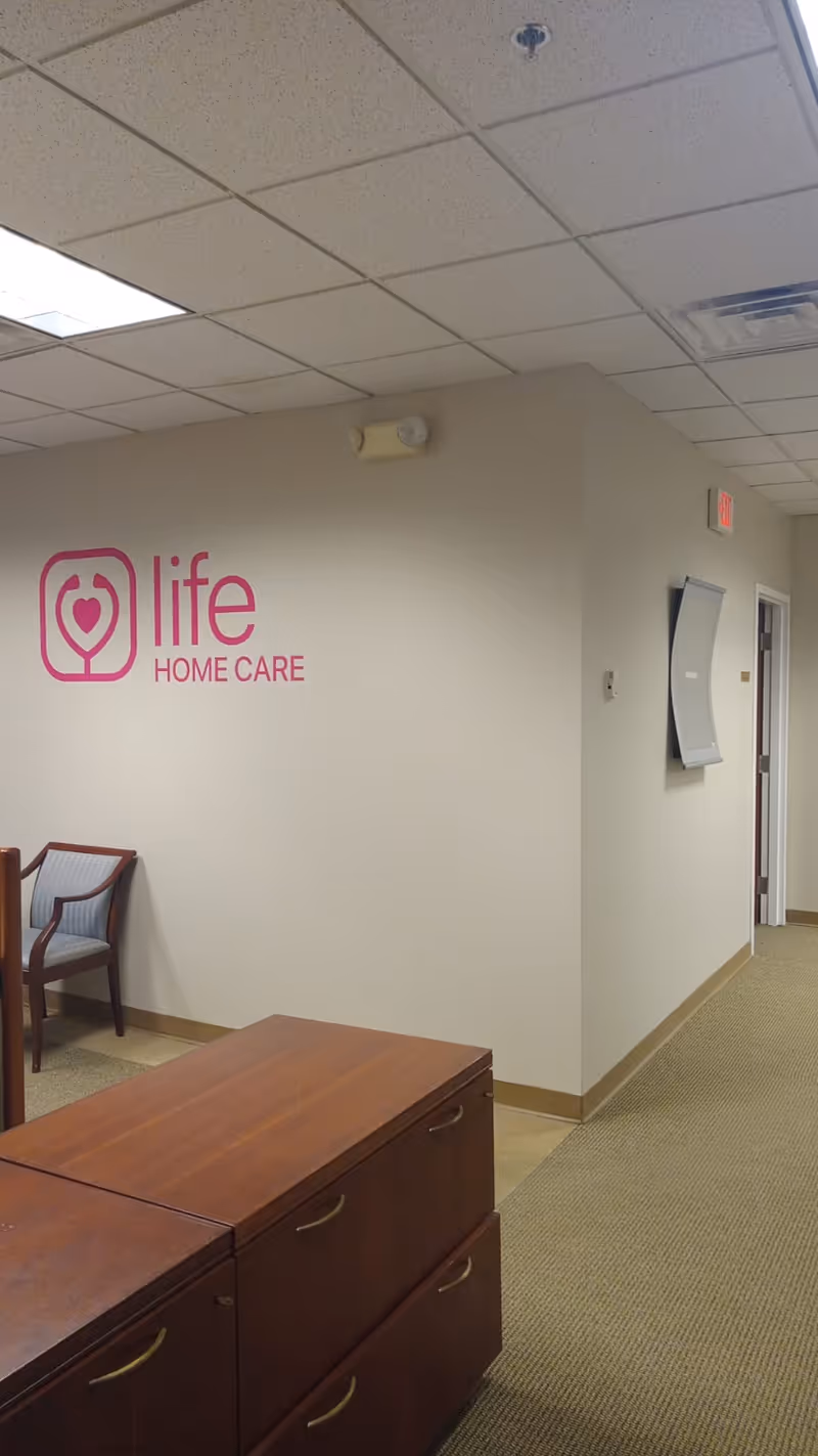 Interior hallway with Life Home Care logo on the wall, chairs, and wooden desks.