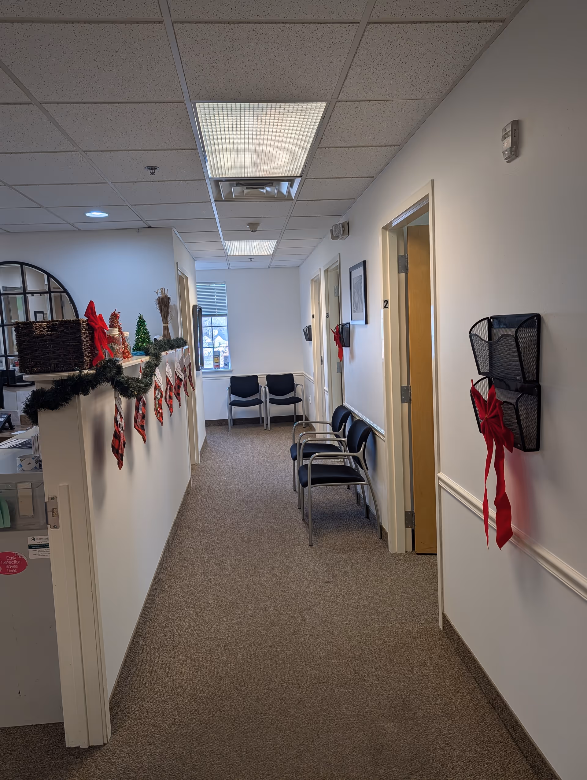 Interior hallway of a senior living facility decorated for Christmas with chairs along the wall.