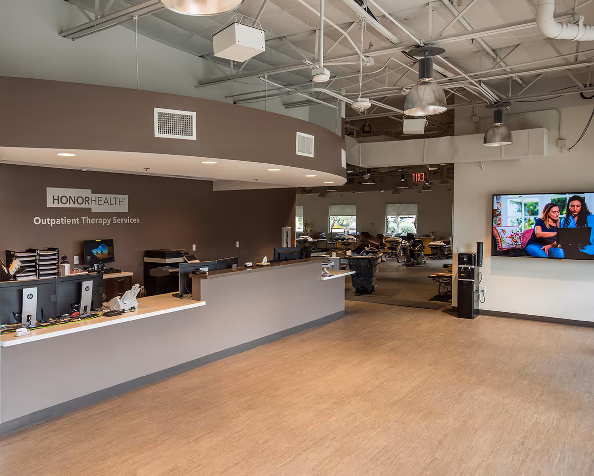 HonorHealth outpatient therapy reception with curved counter, computers, and a large wall-mounted screen.