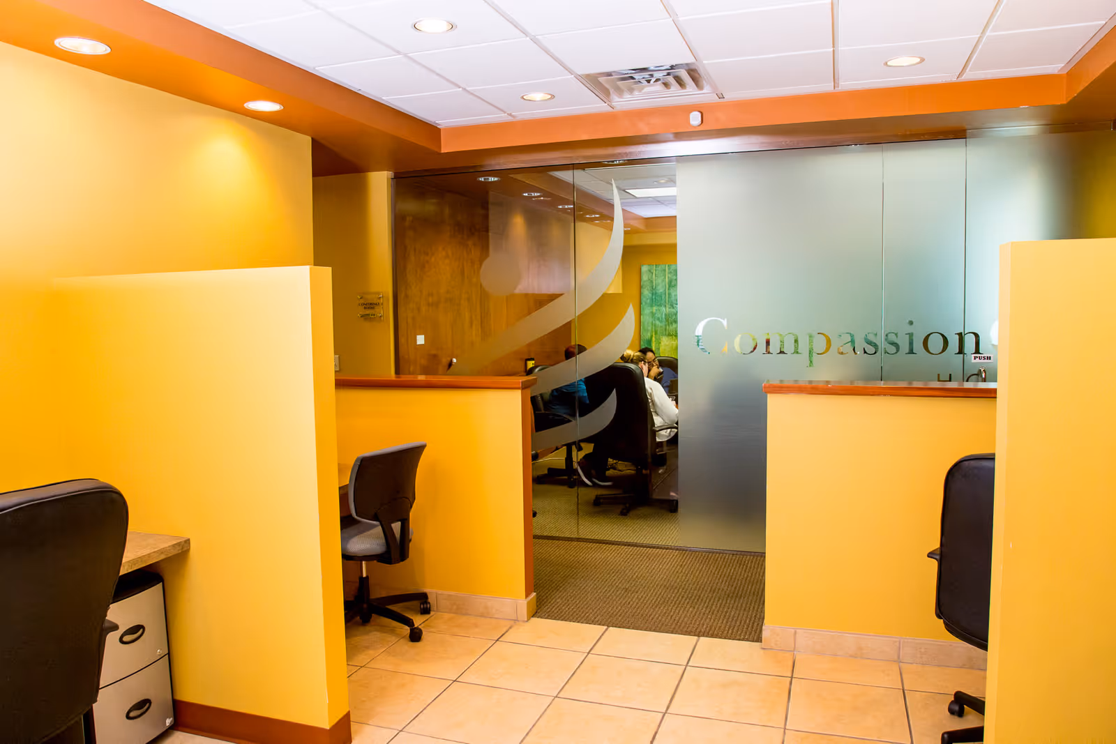 Reception area with yellow walls, glass doors reading Compassion, and office chairs.