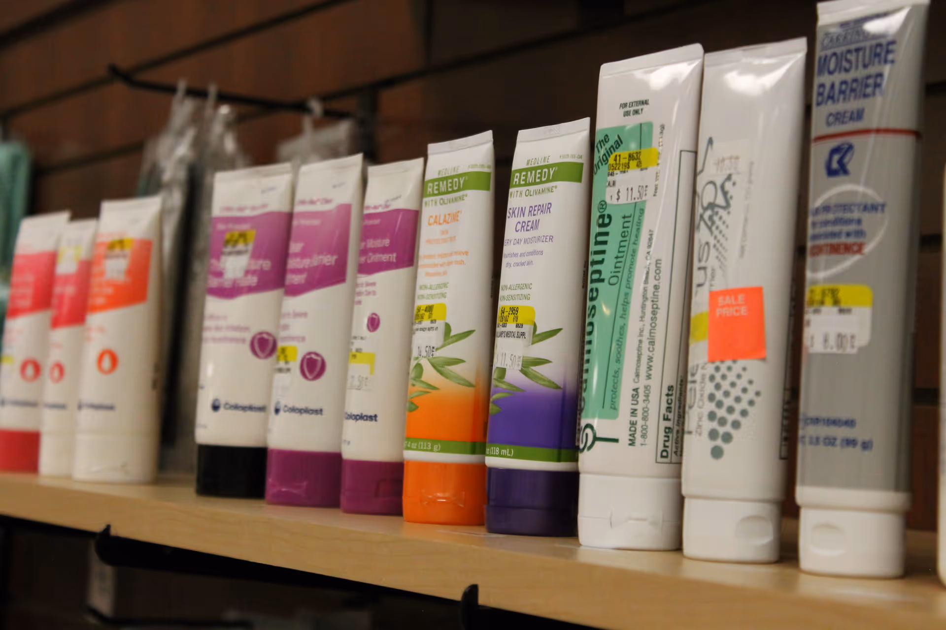 Row of assorted medical ointment tubes lined up on a wooden shelf.