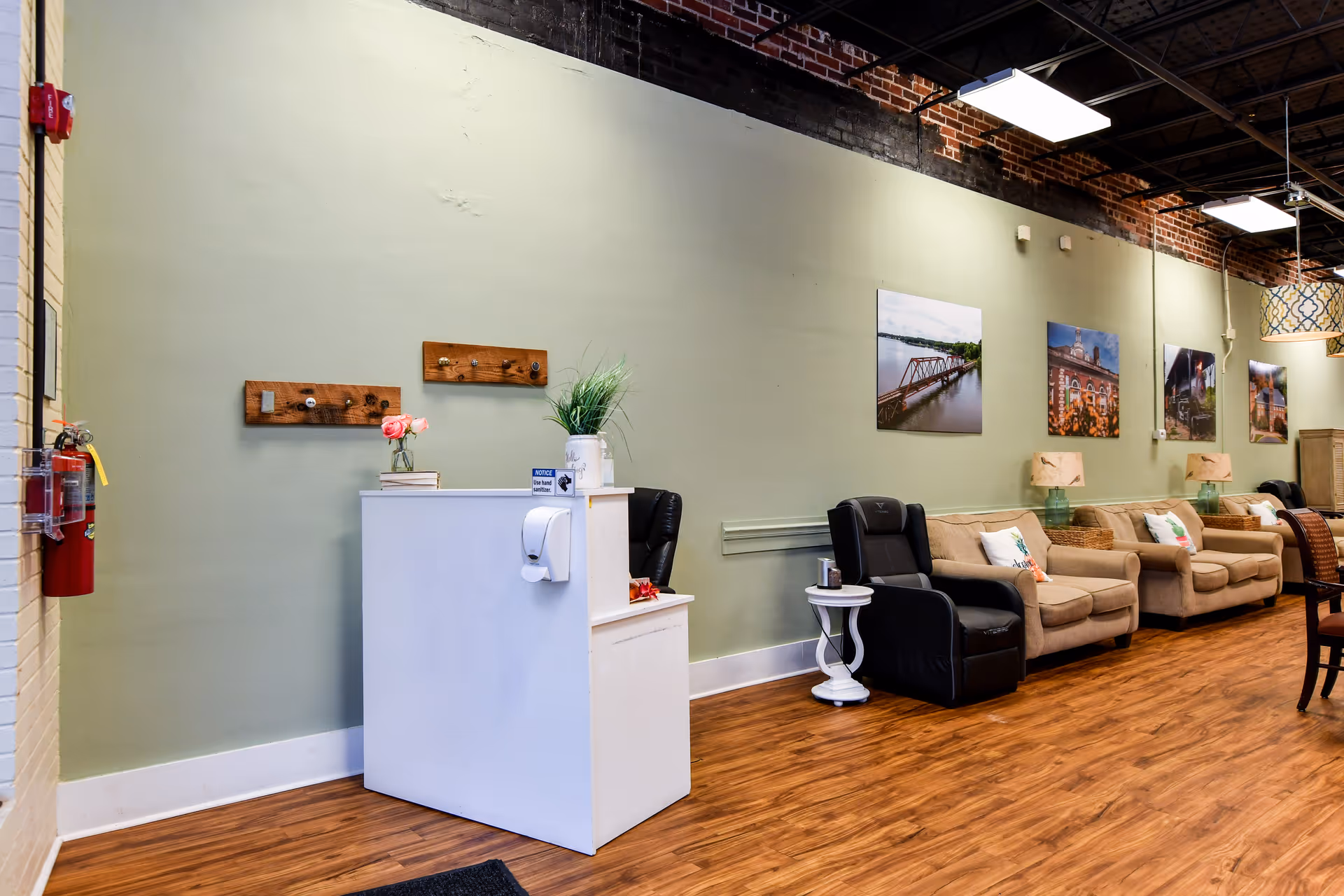 Lounge lobby with beige couches, black recliners, a white reception desk, and wall art.