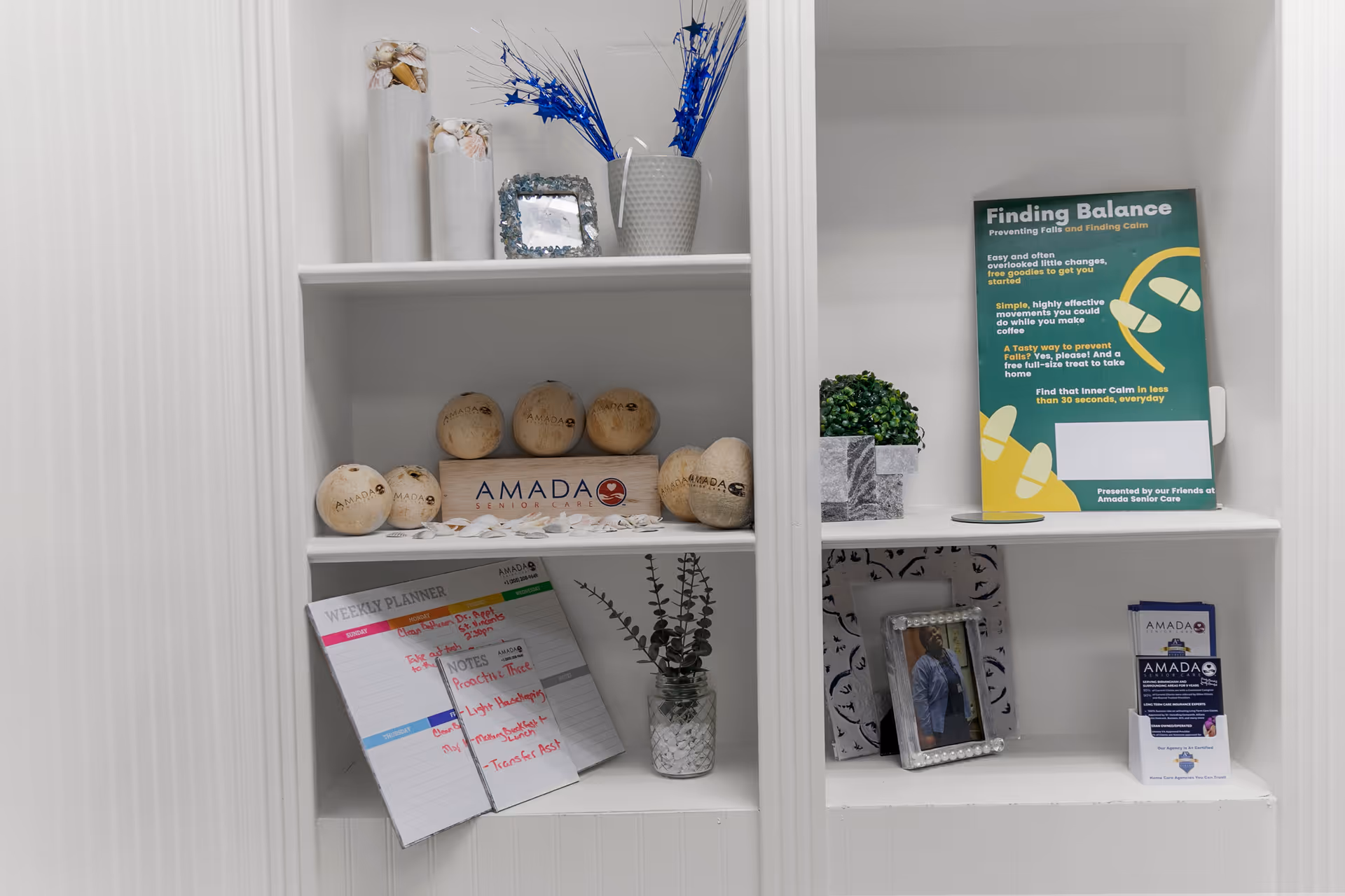 Shelves displaying decor, a weekly planner, plants, framed photos, and Amada Senior Care brochures.