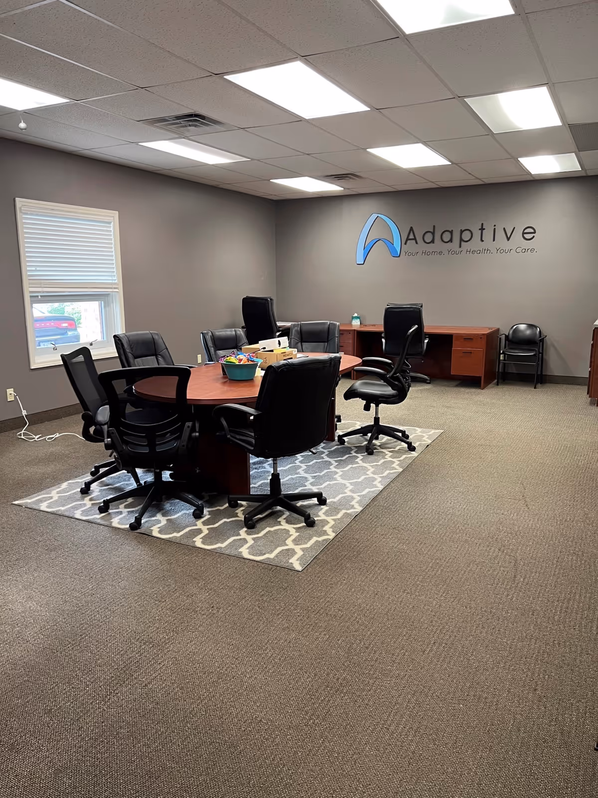 Meeting room with a large oval conference table, multiple chairs, and Adaptive logo on wall.