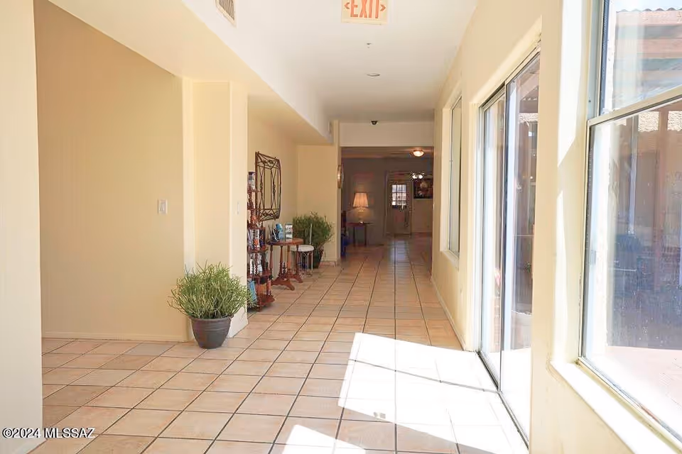 Sunlit beige hallway of a senior living facility with tiled floor, plants, and glass doors.