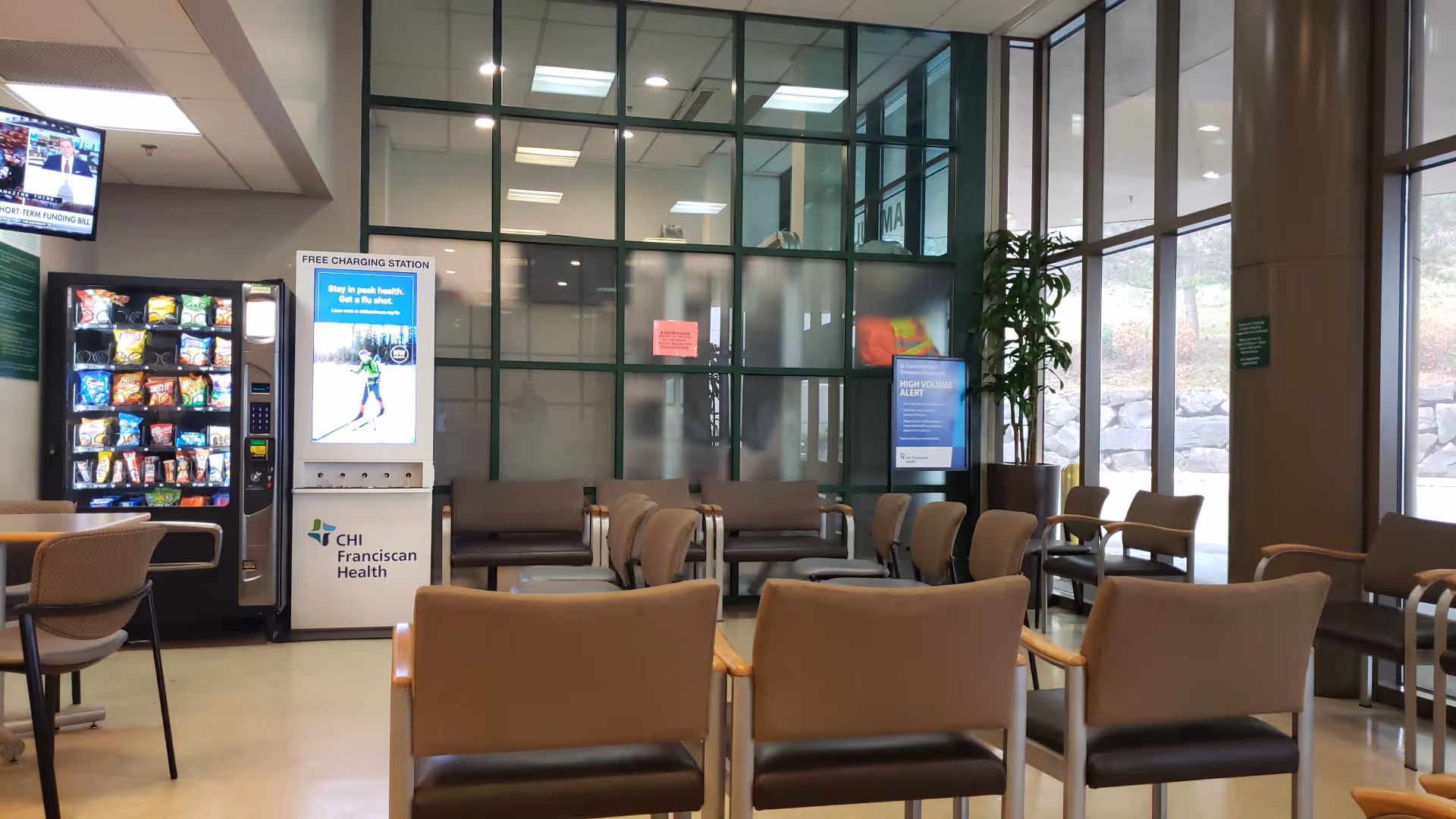 Lobby seating area with chairs, vending machine, glass walls, and potted plant.
