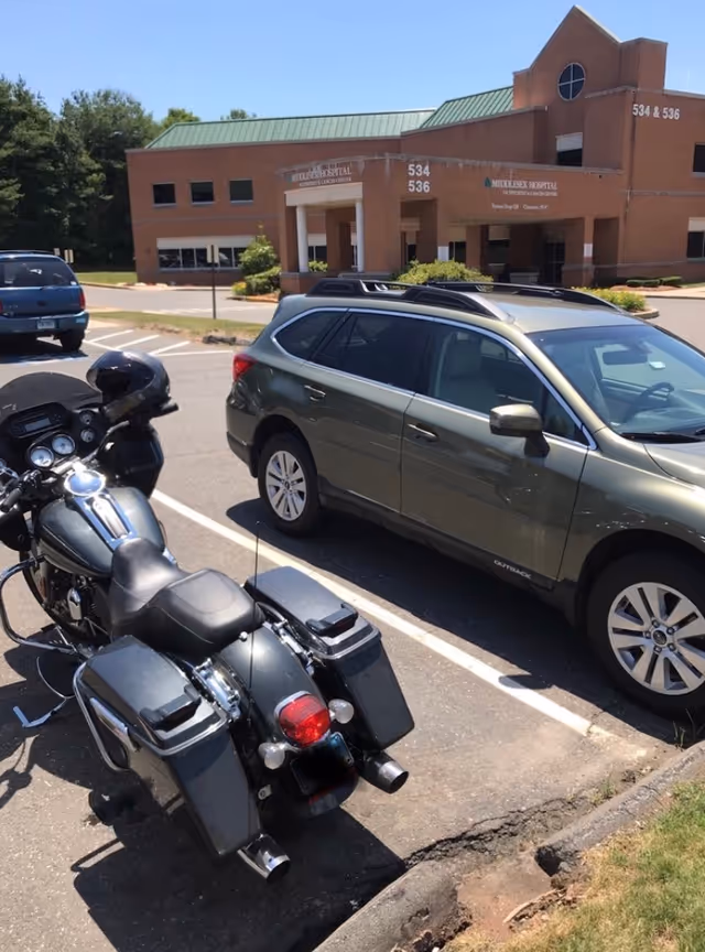 Exterior view of a brick hospital building with cars and motorcycles in the parking lot.
