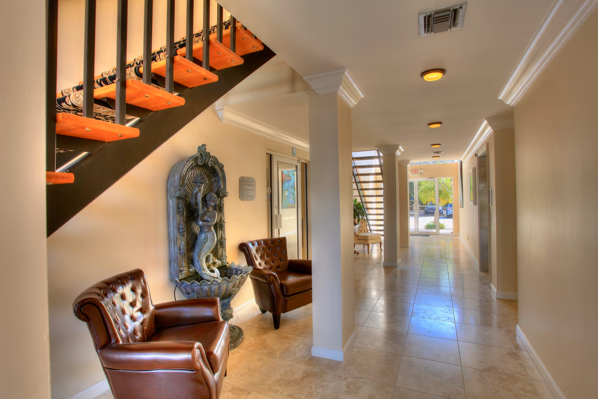 Long beige hallway in a senior living facility with staircase, chairs, and sculpture.